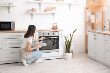Fototapeta na wymiar Young woman opening electric oven in kitchen