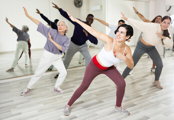 Obraz premium Positive sporty young Hispanic woman practicing modern vigorous dance movements in group dance class