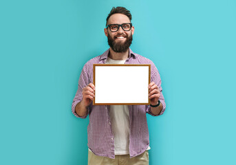 A handsome guy with a beard in eyeglasses proudly holds in his hands a frame with an empty space for your diploma, award or text. Recognition for good work