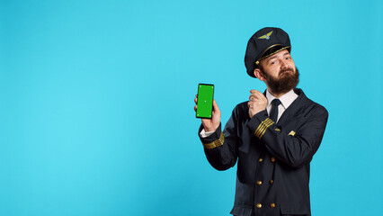 Positive aircrew captain showing phone with greenscreen, holding smartphone with isolated display...