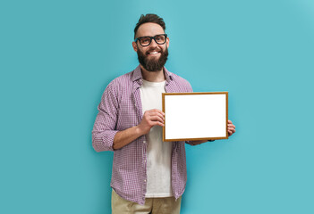 A handsome guy with a beard in eyeglasses proudly holds in his hands a frame with an empty space...