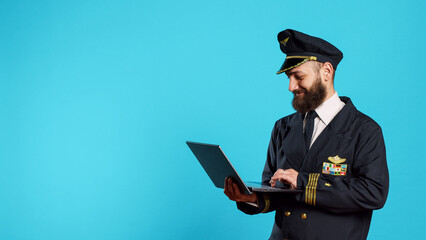 Modern aircrew captain using laptop on camera, browsing online website and social media app. Male pilot working on commercial flights and holding wireless computer, navigating internet.