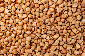 Buckwheat groats raw, brown seeds, small grains in bulk close-up, background wallpaper, uniform texture pattern