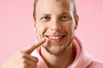 Young bearded man pointing at his teeth on pink background, closeup