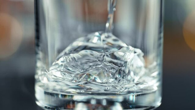 Super Slow Motion Detail Shot of Pouring Transparent Alcohol Liquid into Glass with Ice at 1000fps.