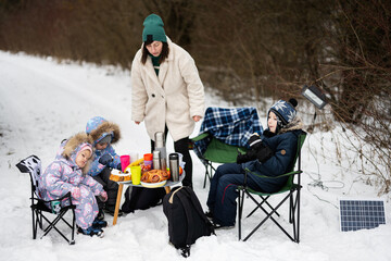 Young woman with children in winter forest on a picnic. Mother and three kids.