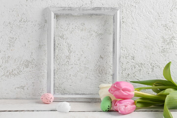 Empty picture frame, tulip flowers and Easter eggs on wooden table near light wall