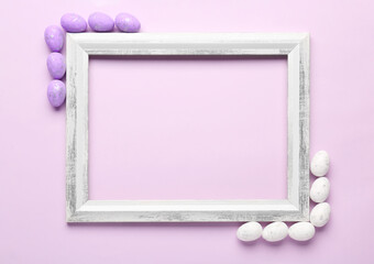 Composition with empty picture frame and Easter eggs on lilac background