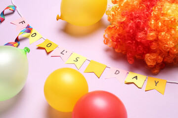 Text FOOL'S DAY, balloons and clown wig on lilac background, closeup