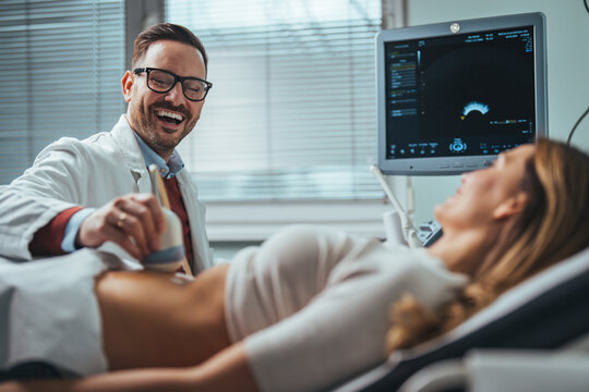 Doctor using ultrasound and screening woman's stomach. Pregnant woman getting ultrasound from doctor. Side view portraits of gynecologist in white lab coat using ultrasound scanner 