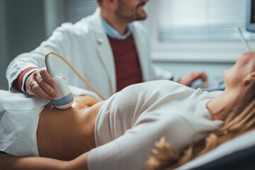 Selective focus on ultrasound scanner device in the hand of a professional doctor examining his patient doing abdominal ultrasound scanning sonogram sonography sonographer early pregnancy