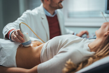 Selective focus on ultrasound scanner device in the hand of a professional doctor examining his patient doing abdominal ultrasound scanning sonogram sonography sonographer early pregnancy - Powered by Adobe