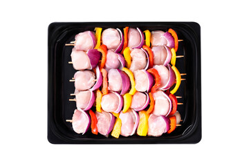 Raw chicken skewers of fillet with vegetables, plums, peppers, onions, in a tray on a white background.Skewers with pieces of raw meat, red, yellow and green pepper. Close-up.Top view.