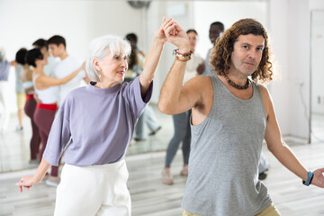 Happy caucasian guy and old lady practising paired latin dance in dance studio