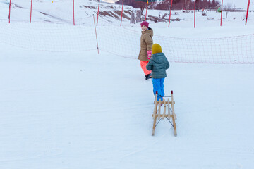 two children pulling the wooden sledge on snow slope