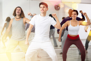 Fototapeta premium Smiling dark-haired young guy attending group choreography class, learning modern dynamic dances. Concept of active lifestyle ..