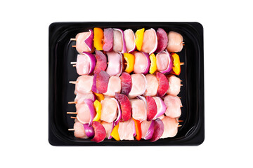 Raw chicken skewers of fillet with vegetables, plums, peppers, onions, in a tray on a white background.Skewers with pieces of raw meat, red, yellow and green pepper. Close-up.Top view.