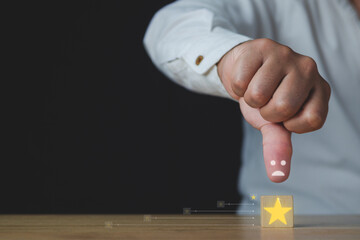 The man shows thumbs down or dislike. That is an evaluation. A cube has a star that means a bad job and service for customer review. Close up shot with copy space. Isolated on black background.