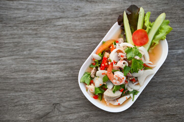 mixed salad with shrimp squid pork sausage with fresh vegetable cucumber celery leaf on plate on wooden table, Thai food salad