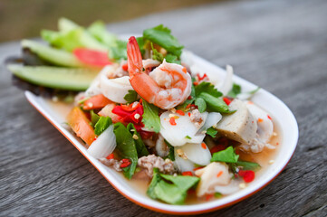 mixed salad with shrimp squid pork sausage with fresh vegetable cucumber celery leaf on plate on wooden table - Thai food salad
