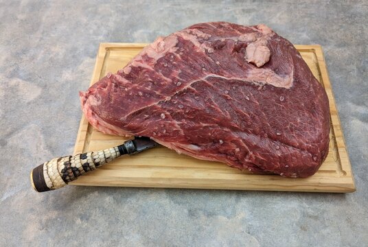Raw picaña wagyu meat, traditional knife, wooden plate and salt on cement background