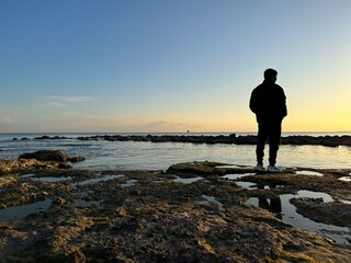 Fototapeta premium Man looking towards the sunset on the seashore in winter