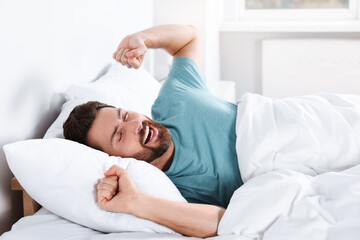 Happy man stretching on comfortable pillow in bed at home