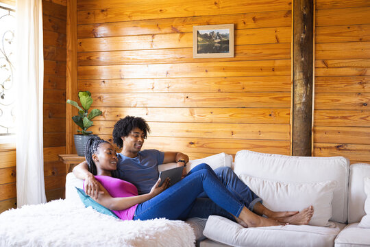 Happy african american couple spending time in log cabin using tablet