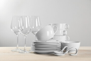 Set of clean dishware and glasses on white wooden table against light background