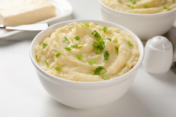 Bowls of delicious mashed potato with green onion on white table