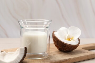 Glass of delicious vegan milk, coconut pieces and flower on white wooden table