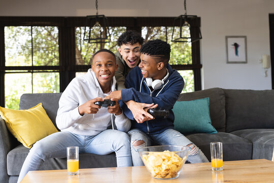 Image of happy diverse male teenage friends playing video games at home