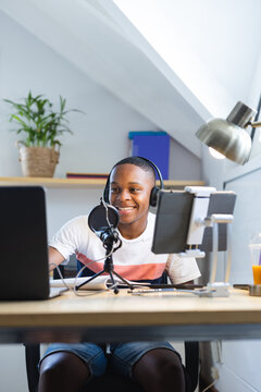 Vertical image of happy african american teenager with headphones and microphone recording podcast