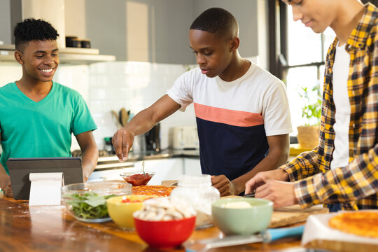 Happy diverse teenage male friends preparing pizza in kitchen