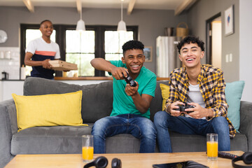 Happy diverse teenager male friends playing video games at home