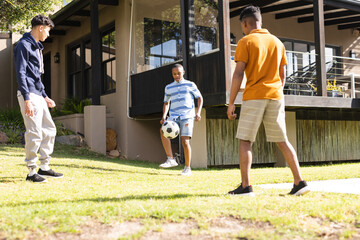Happy diverse teenager male friends playing soccer in backyard