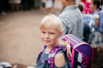 Erstklässlerin mit Rucksack am ersten Schultag, die direkt in die Kamera schaut