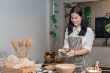 View of Asian woman wearing apron and  Sifting Bread Flour before the process of Kneading Dough.