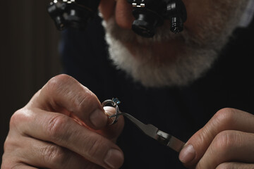 Professional jeweler working with ring on dark background, closeup