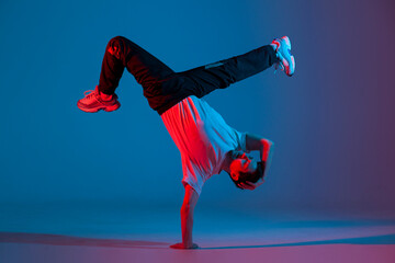young guy dancer break dancing in neon red blue lighting, active energetic man doing acrobatic tricks, crazy moves - obrazy, fototapety, plakaty