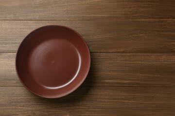 Clean brown plate on wooden table, top view. Space for text