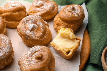 Delicious profiteroles filled with cream on green background, closeup