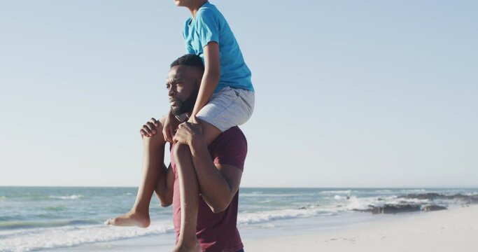 Video of happy african american father and son walking on beach at sunset