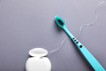 Container with dental floss and toothbrush on light grey background, flat lay