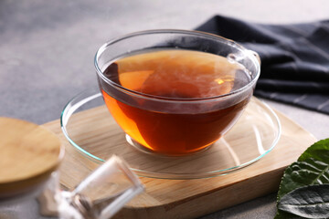 Aromatic hot tea in glass cup and leaves on light grey table, closeup