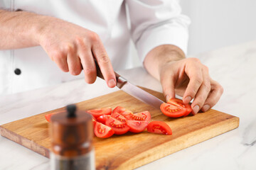 Obraz na płótnie Canvas Chef cutting tomatoes at marble table in kitchen, closeup