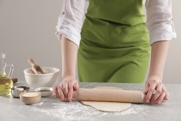 Obraz na płótnie Canvas Woman rolling fresh dough at light grey marble table, closeup. Cooking grissini