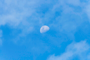 Late afternoon partial moon rising amongst the soft high cloud in the blue sky