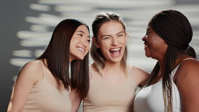 Multiethnic group of models posing for body positivity ad in studio, having fun with friends advertising skincare products. Cheerful women laughing on camera, different skintones and body types.