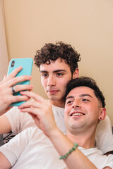 Fototapeta premium Close up of a gay couple lying on the sofa and using the mobile to interact on social media. Daily routine